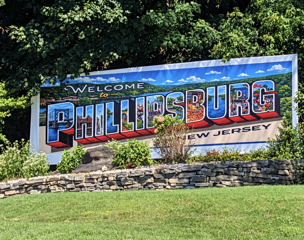 Colorful Welcome to Phillipsburg New Jersey sign mounted on a stone wall beside grass